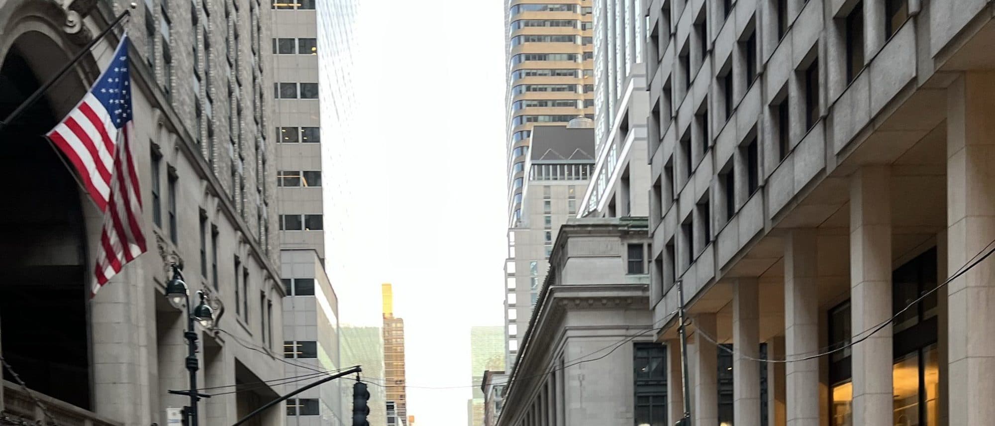 A view down a Manhattan financial district street lined with skyscrapers and an American flag