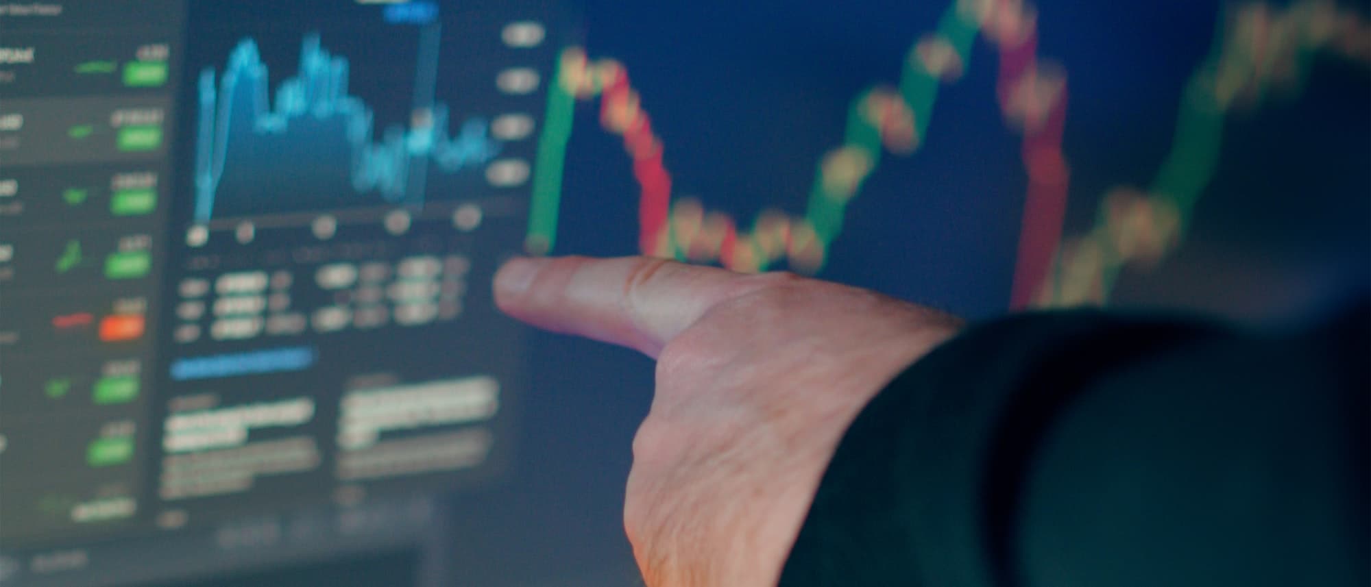 A trader pointing at equity and options price charts on a trading screen